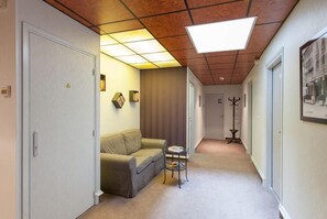 A hallway with a sofa, a small table, and a coat rack. - Marguerite (Dinan)