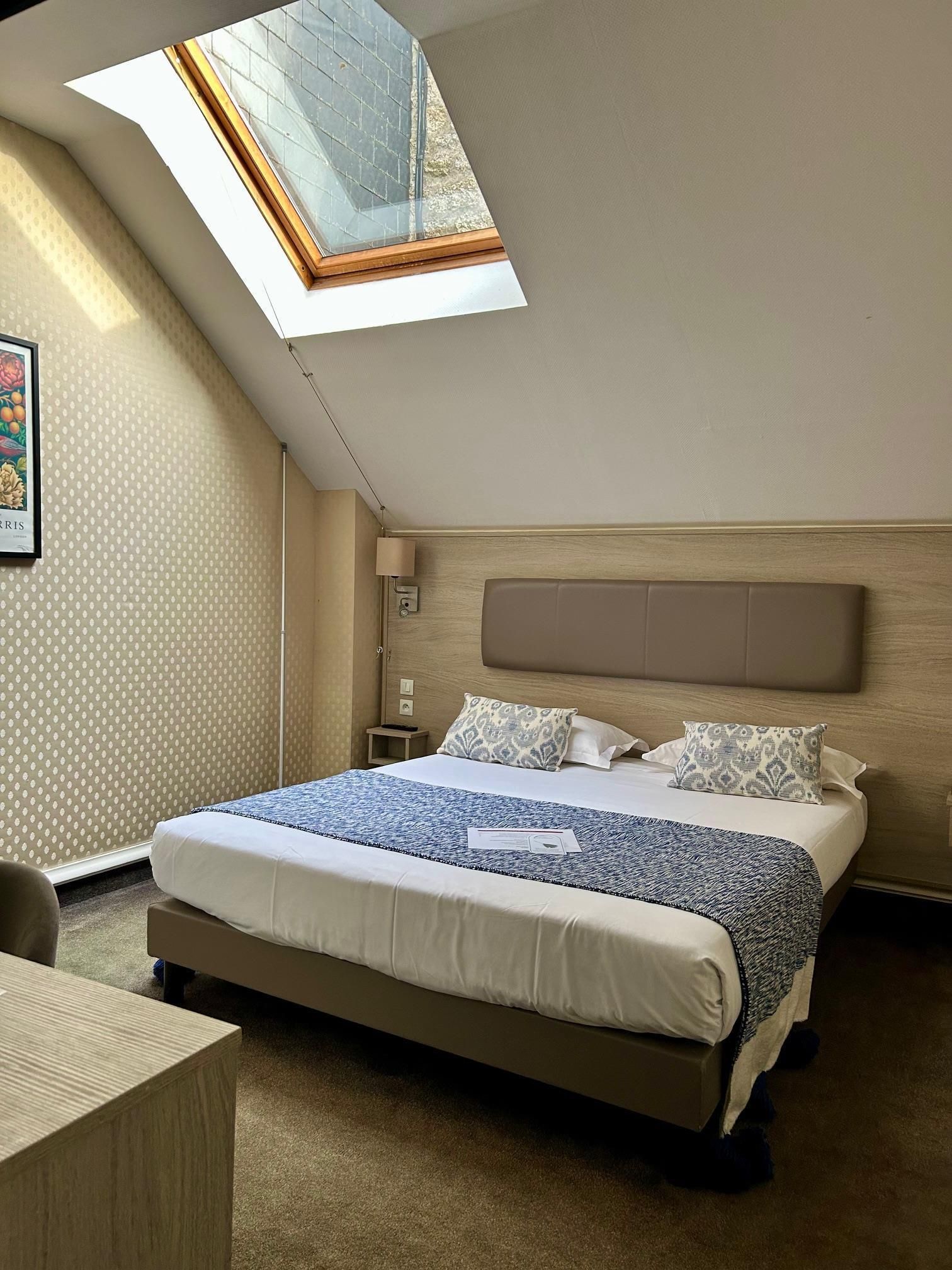 Ein Schlafzimmer mit Oberlicht, einem Bett mit gemusterten Textilien, einem Nachttisch und einer Wandleuchte.