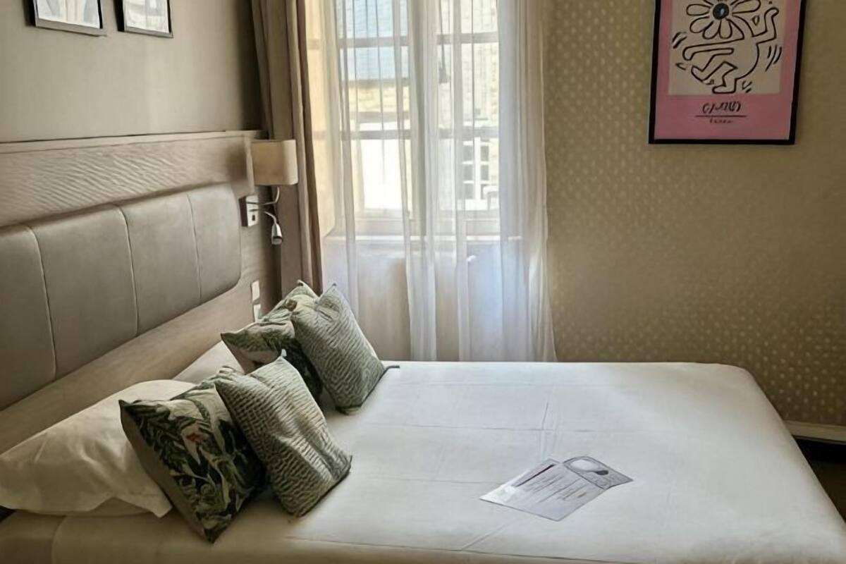 Une chambre d’hôtel avec un lit, des oreillers, une table de chevet, une lampe et une fenêtre avec des rideaux.