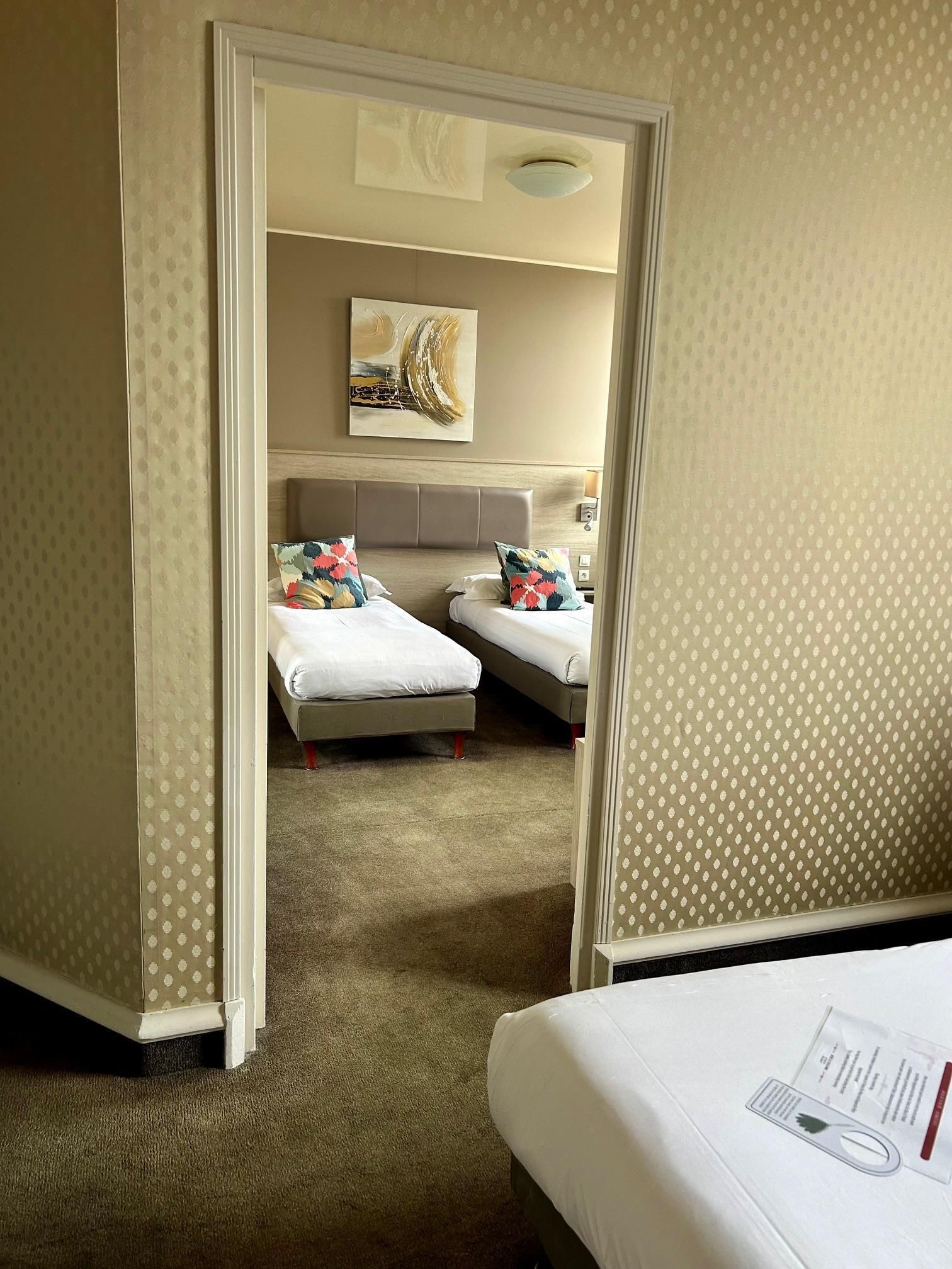 Habitación de hotel con dos camas, una lámpara en el techo, una obra de arte en la pared y piso alfombrado.