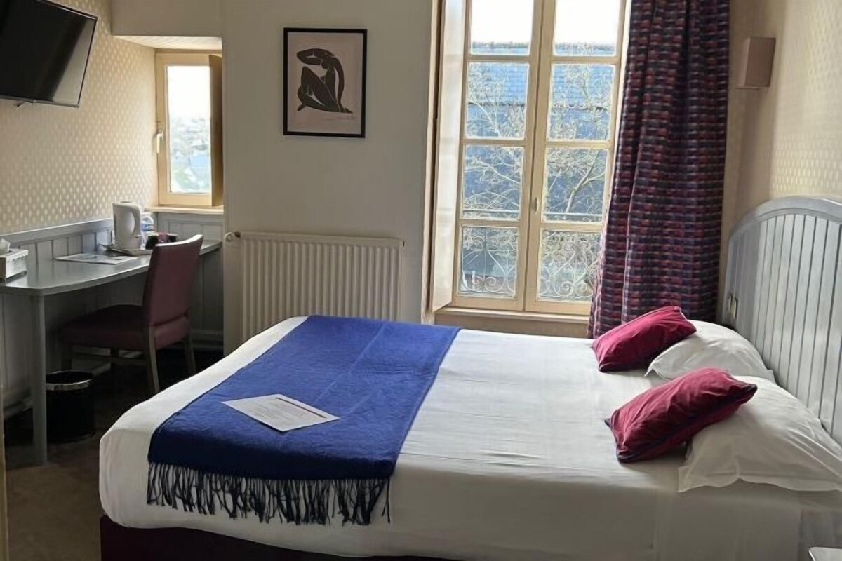 A hotel room with a bed, a desk, a chair, a window with a view, and a television mounted on the wall.