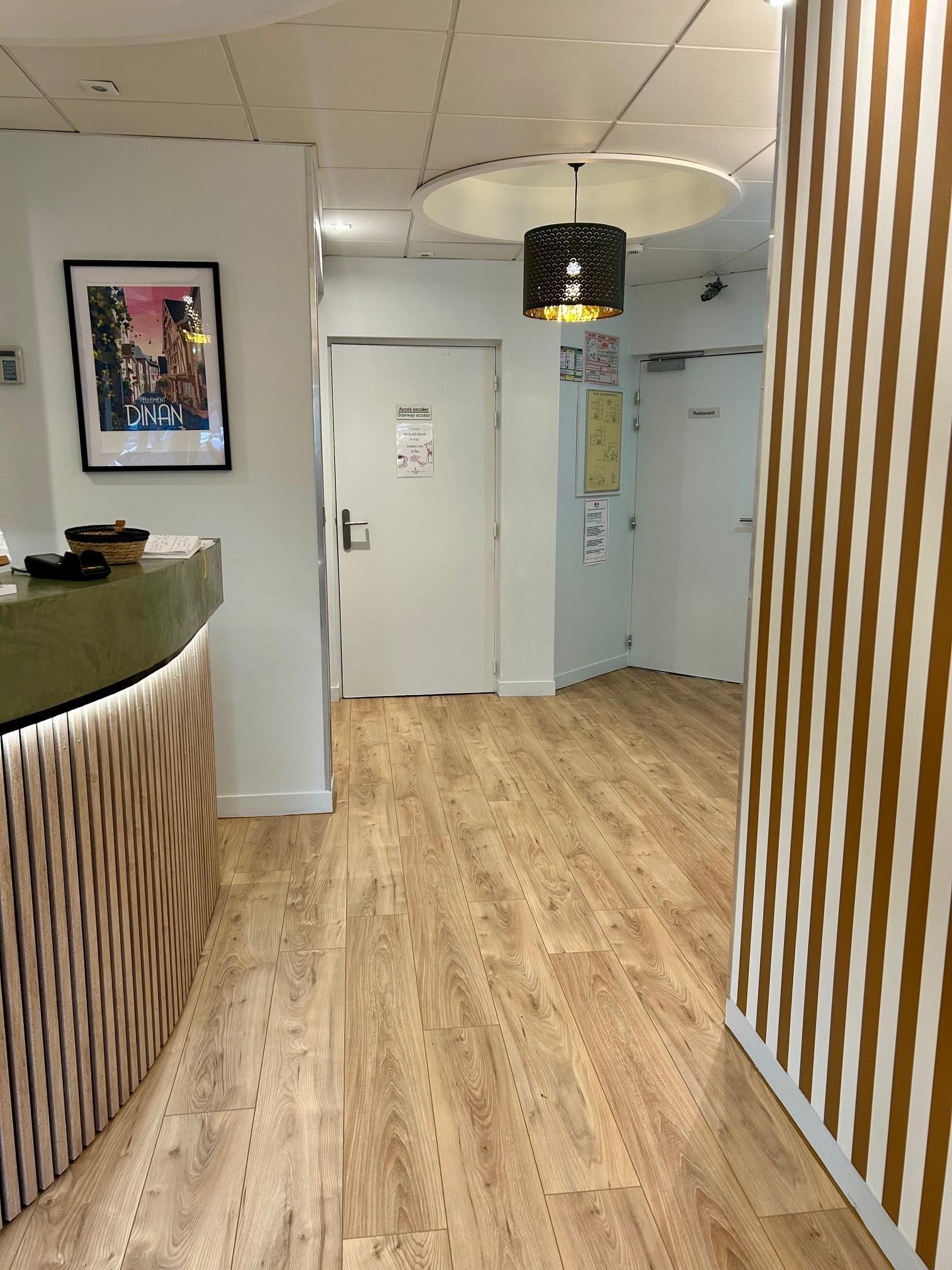 A reception area with a wooden reception desk, a framed cityscape picture, a door with a notice, and a hanging light fixture.