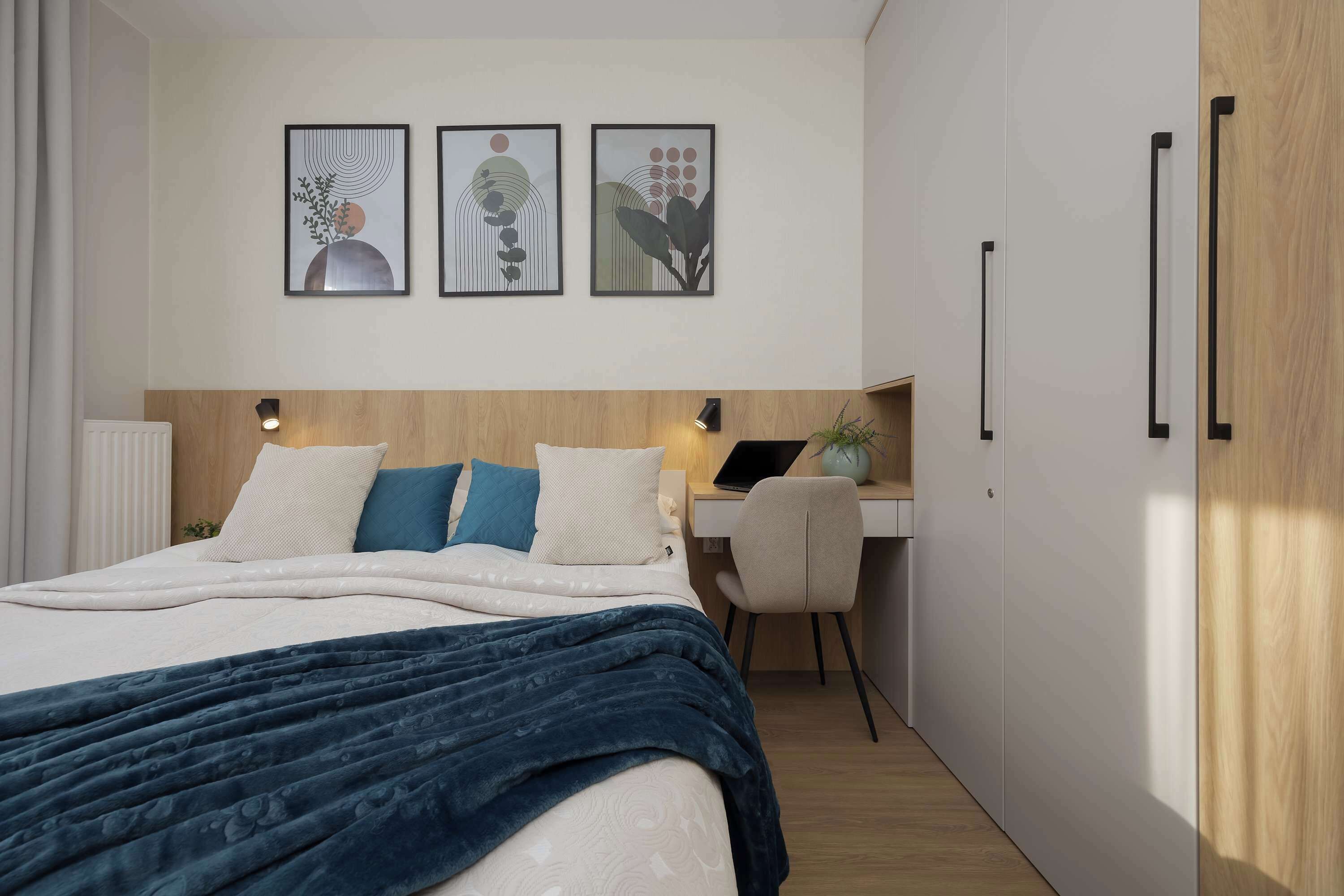 Een moderne slaapkamer met een groot bed, een bureau en een computer. Drie kunstwerken hangen in lijsten aan de muur.
