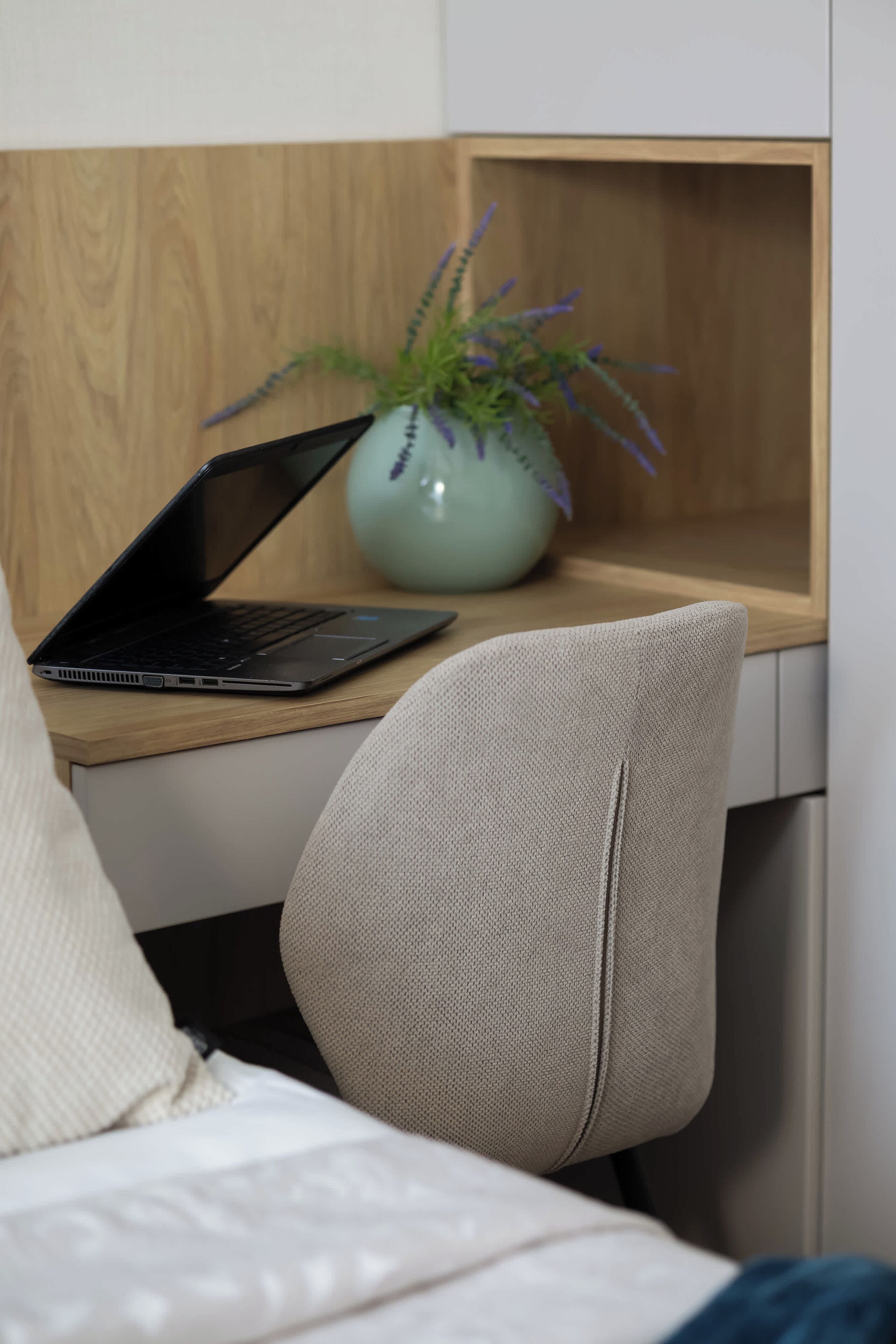 A laptop on a wooden desk with a potted plant beside it.