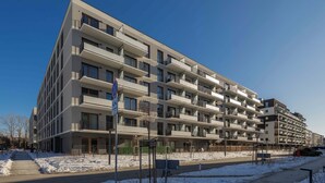En flervåningsbyggnad med lägenheter och balkonger, en klar himmel och ett snötäckt markområde.
