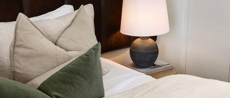 A neatly made bed with a beige comforter and pillows, a dark brown upholstered headboard, and a table lamp with a white shade.