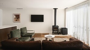 Un soggiorno moderno con divano, poltrone, televisore, camino e un'ampia finestra con tende leggere.