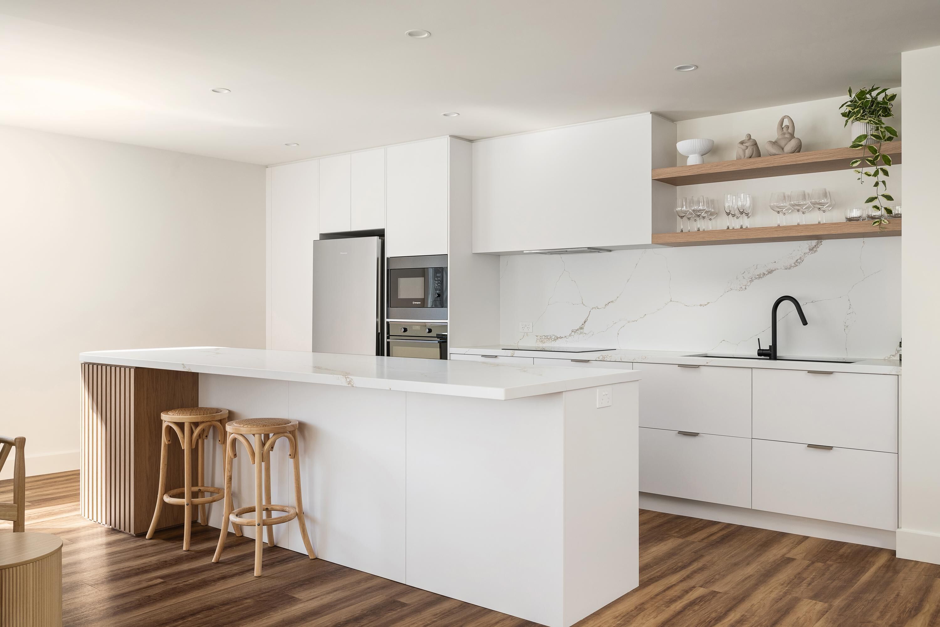 Una cocina moderna con armarios blancos, salpicadero de mármol y una isla central con taburetes.