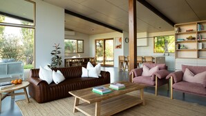 A modern living room with a brown leather sofa, a wooden coffee table with books, and a pink sofa. - Silver House, Ground Floor - Mt Buffalo Rd - Alpine Haven on Mount Buffalo Road – A Spacious Retreat for Families, Friends & Nature Lovers (Porepunkah)