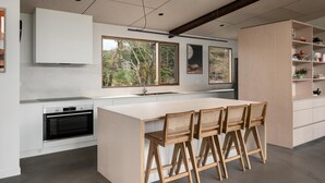 A modern kitchen with a central island, built-in oven, and large windows offering views of trees. - Silver House, Ground Floor - Mt Buffalo Rd - Alpine Haven on Mount Buffalo Road – A Spacious Retreat for Families, Friends & Nature Lovers (Porepunkah)