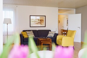 A living room with a sofa, a yellow armchair, a small wooden table, and a framed picture on the wall. - Apartment Alm-Atelier, stylish, quiet, private terrace, Wi-Fi, near forest and vineyards (Durbach)