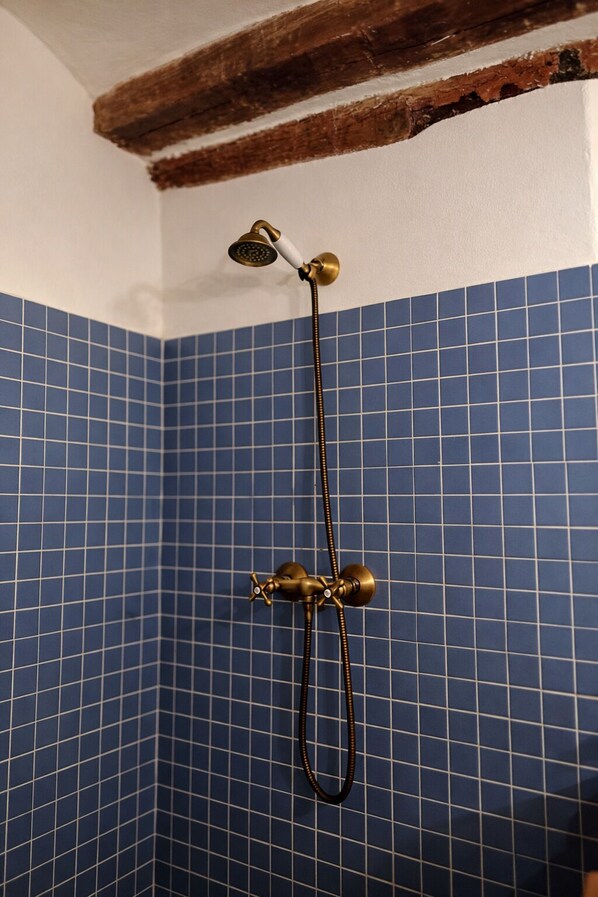 Esquina de un baño con paredes de azulejos azules y una ducha con accesorios de latón.