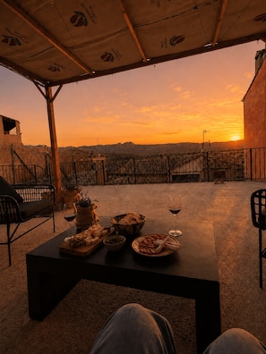 An outdoor seating area with a table set for a meal, a view of the sunset, and a building in the background.