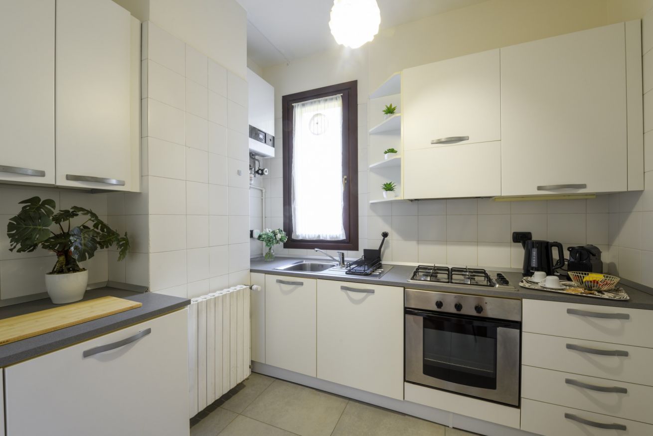 Een moderne keuken met witte kastjes, een gasfornuis, een oven en een raam met gordijn.