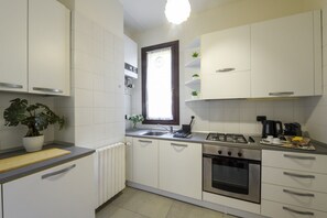 A modern kitchen with white cabinets, a gas stove, an oven, and a window with a curtain. - Borromei, 11 - Elegance in the City Center (Milan)