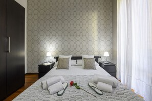 Habitación de hotel con una cama grande, dos mesitas de noche, un armario y una pared con diseño.