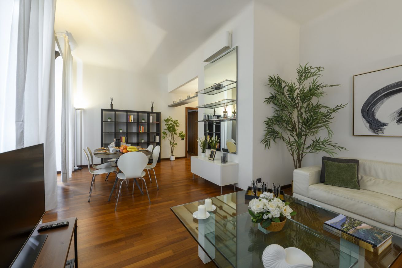 A modern living room with a glass coffee table, white sofa, and a dining area with chairs and a small table.