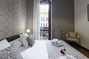 A hotel room with a bed, a chair, a table with towels, and a view of buildings through a window. - Borromei, 11 - Elegance in the City Center (Milan)