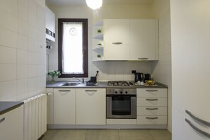 A compact kitchen with white cabinets, a gas stove, an oven, a window with a curtain, and a radiator. - Borromei, 11 - Elegance in the City Center (Milan)