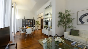 Una sala de estar moderna con una mesa de centro de vidrio, un sofá blanco y una zona de comedor con sillas y una pequeña mesa.