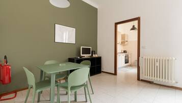 Zona pranzo con tavolo e sedie, estintore, televisore su un mobile e cucina visibile attraverso una porta aperta.