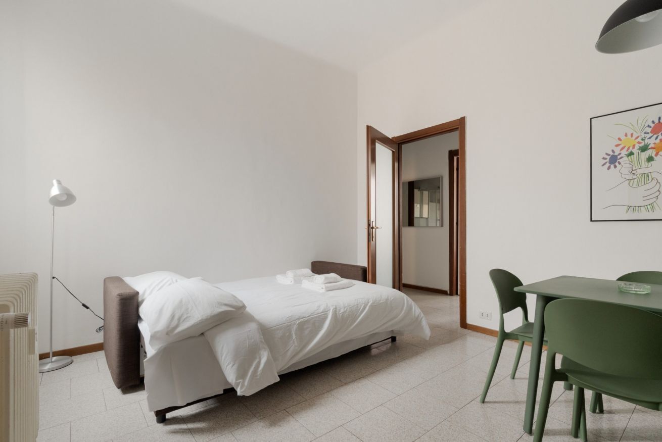 A bedroom with a bed, a desk, and a chair. There is a door leading to another room.