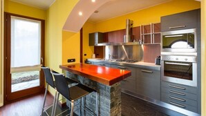 A modern kitchen with a stone island, stainless steel appliances, and a yellow accent wall.