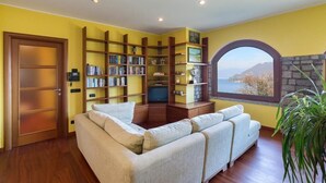 A living room with a sofa, wooden bookshelves, a television, and a view of a lake through a window.