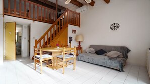 Een kamer met een houten trap, een eettafel met stoelen, een bank en een klok aan de muur.