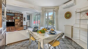 A dining area with a table set for two, a kitchen with wooden cabinets and a built-in oven, and a view of the outdoors through large windows. - Thai House Private Parking Near Lake (Toscolano Maderno)