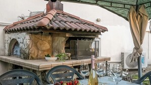 An outdoor dining area with a stone-built grill, a table set with a fruit bowl, wine glasses, and a bottle. - Thai House Private Parking Near Lake (Toscolano Maderno)