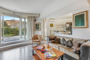 A living room with a sofa, armchairs, a coffee table with books and a bottle, and a view of the outside. - Thai House Private Parking Near Lake (Toscolano Maderno)