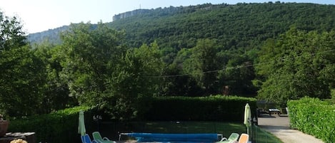 A swimming pool with lounge chairs, surrounded by greenery and a hilly landscape.