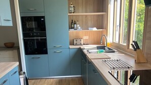 Eine moderne Küche mit blauen Schränken, einer Edelstahl-Dunstabzugshaube, einem Einbauofen und einem großen Fenster für natürliches Licht.