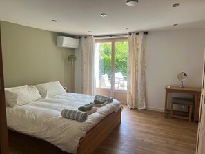 Ein Schlafzimmer mit einem Bett, einem Nachttisch mit Spiegel und Blick auf einen Außenbereich mit Sitzgelegenheiten.