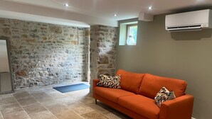 Ein Zimmer mit Steinwand, einem orangefarbenen Sofa, einer blauen Matte und einem kleinen Fenster.