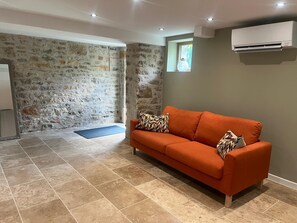 Ein Zimmer mit Steinwand, einem orangefarbenen Sofa, einer blauen Matte und einem kleinen Fenster.