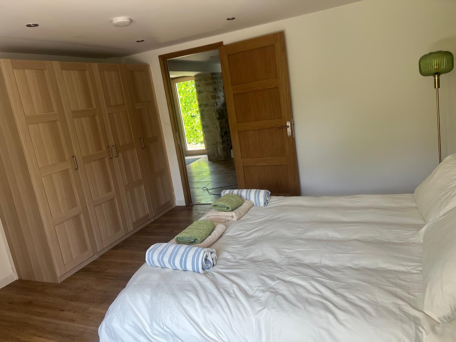 Une chambre avec un grand lit, une armoire en bois et une porte donnant sur un balcon.