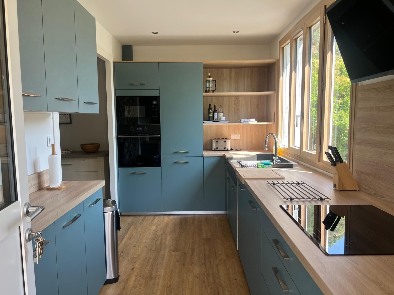 A modern kitchen with blue cabinets, a built-in oven, a sink, and a window providing natural light.