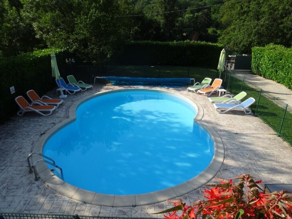A swimming pool with a tiled deck, surrounded by lounge chairs and a green fence.