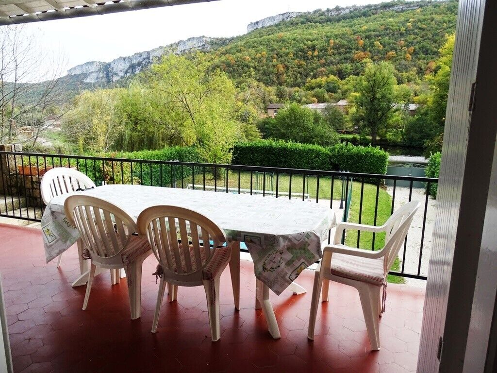 An outdoor patio with a table and chairs, overlooking a mountainous landscape and a body of water.