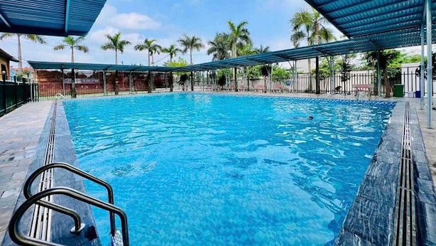A swimming pool with a covered area, palm trees, and a clear sky. - Palette Sunset Garden Tam Coc (Ninh Binh)