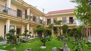 A hotel courtyard with a well-maintained lawn, rock garden, and a two-story building with balconies. - Palette Sunset Garden Tam Coc (Ninh Binh)