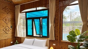 A bedroom with a bed, bedside table, lamp, and a large window with curtains. - Palette Sunset Garden Tam Coc (Ninh Binh)