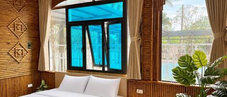 A bedroom with a bed, bedside table, lamp, and a large window with curtains.