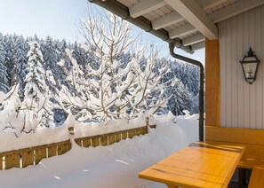 Une terrasse en bois avec un banc, entourée d’arbres couverts de neige.