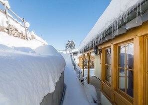 Uma trilha coberta de neve que leva a um edifício com portas e janelas de madeira.