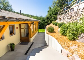 A building with a yellow facade, a wooden staircase leading to a door, and a stone wall with a car parked on it. - Holiday Home 'Ferienhaus Apfelbäumchen Lenzkirch' with Mountain View, Private Terrace and Wi-Fi (Lenzkirch)