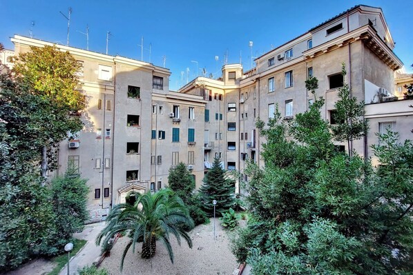 A courtyard with a palm tree and various shrubs, surrounded by multi-story buildings with balconies and air conditioning units. - Lovely Rhome  apartment near Vatican (ROMA)
