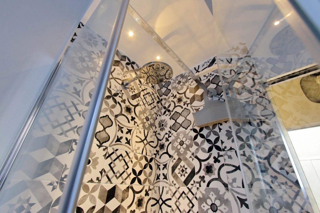 Une douche avec un carrelage aux motifs géométriques et une paroi en verre.